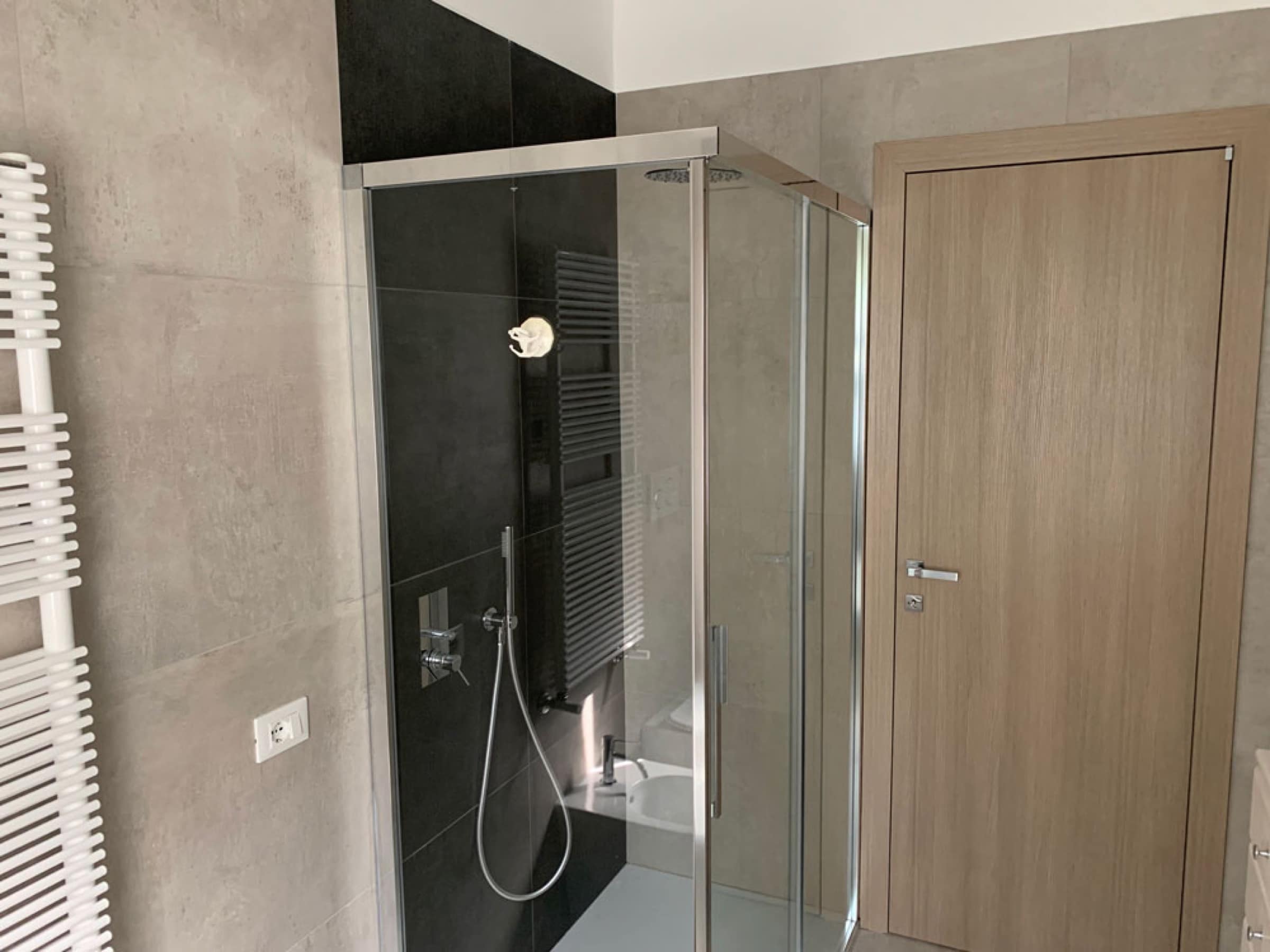 Bagno con box doccia nero e porta in legno